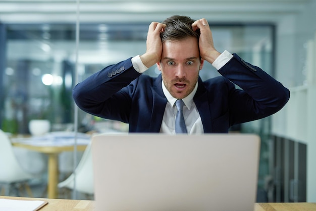 Nunca há um bom momento para o seu laptop travar Foto de um empresário estressado sentado em choque enquanto trabalhava em um laptop em um escritório