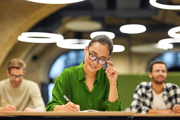 Nunca pare de aprender uma mulher asiática focada usando óculos fazendo algumas anotações enquanto estudava com