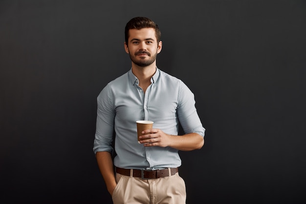 Nur eine Minute, um sich zu entspannen, fröhlicher junger bärtiger Mann, der eine Tasse heißen Kaffee hält