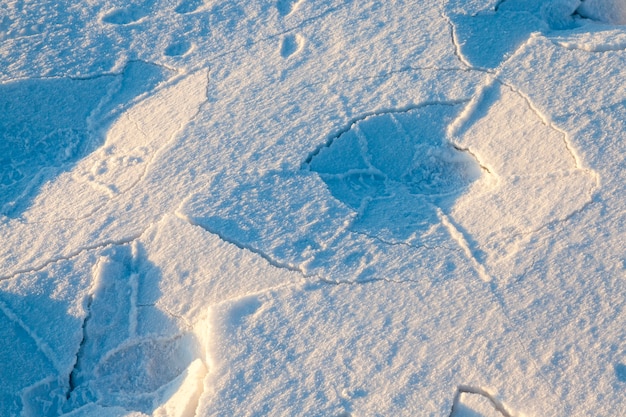 Nur wenige Spuren von Herrenschuhen im Schnee. Auf dem Schnee gibt es Schatten und Risse. Fotografierte Nahaufnahme.