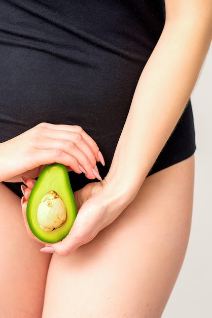 Foto nutrição saudável e conceito de gravidez jovem mulher segurando metade de uma fruta de abacate perto de sua barriga sobre um fundo branco