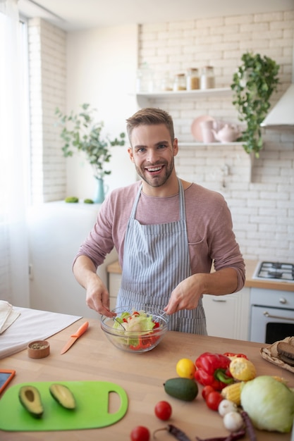 Nutrição saudável. Um homem animado misturando uma salada fresca da estação