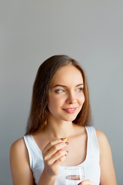 Nutrición Dieta Saludable. Retrato de hermosa mujer joven sonriente tomando píldoras de vitamina