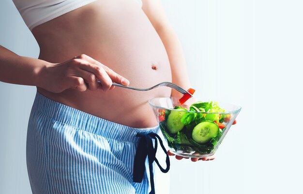 Nutrición saludable y embarazo. Primer plano vientre de mujer embarazada y ensalada de verduras