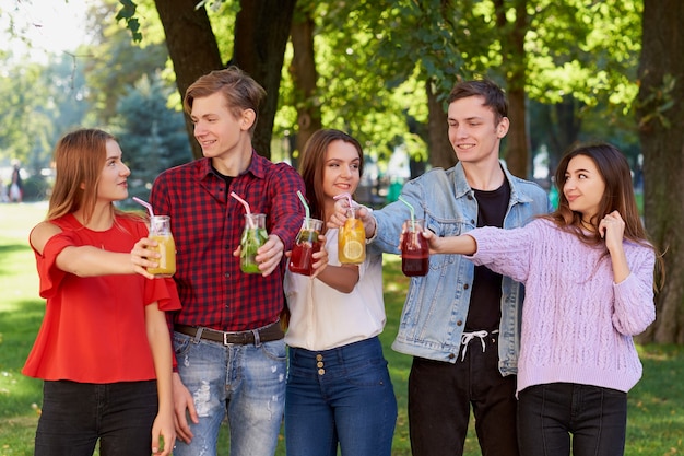 Nutrición saludable. Grupo de amigos bebiendo jugo de desintoxicación fresco sobre fondo verde de la naturaleza.