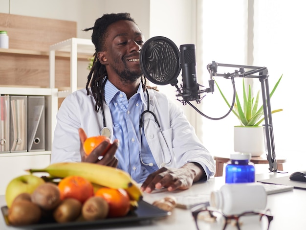 Nutricionista afro-americana olhando para a câmera e mostrando frutas saudáveis na consulta