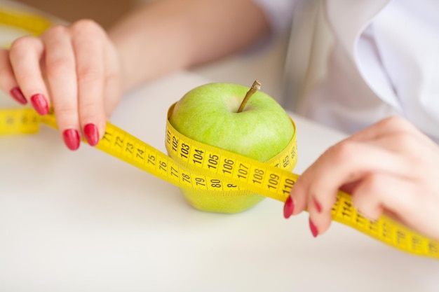 Nutricionista de cerca atando una manzana con una cinta métrica amarilla.