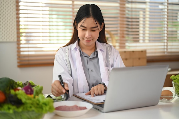 Foto nutricionista em casaco médico branco trabalhando na mesa com legumes frescos e carne crua