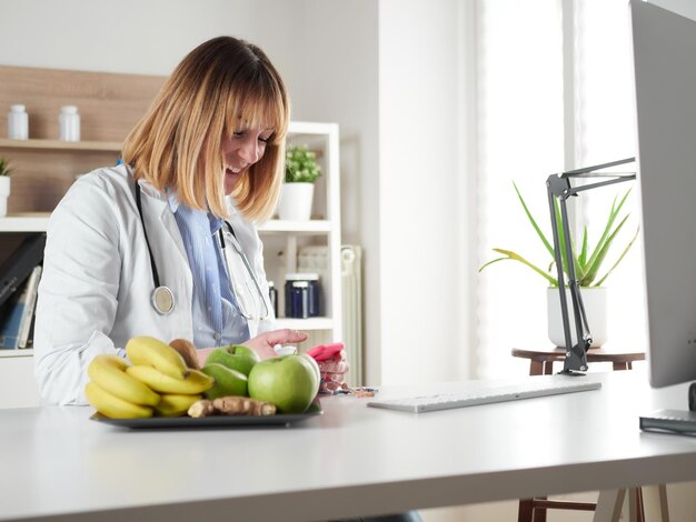 Nutricionista femenina distraída charlando con un teléfono inteligente en el estudio de la oficina