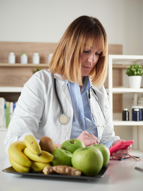 Nutricionista femenina distraída charlando con un teléfono inteligente en el estudio de la oficina