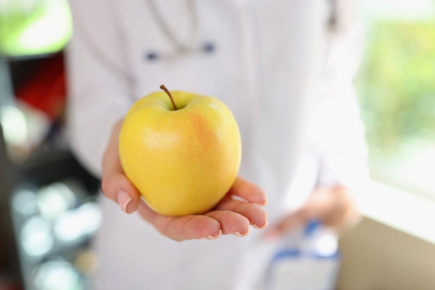 Nutricionista femenina muestra manzana amarilla madura en su mano closeup dieta de alimentos saludables y