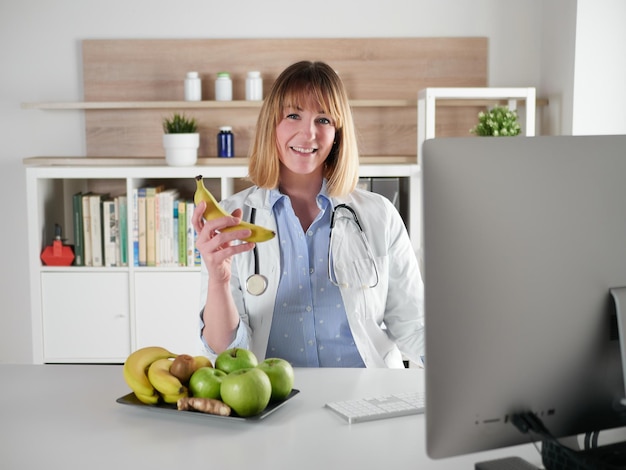 Foto nutricionista femenina sosteniendo una fruta de plátano en el estudio de oficina