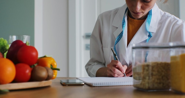 Foto la nutricionista femenina toma nota y los beneficios de los tomates y el brócoli para el plan de comidas de su paciente