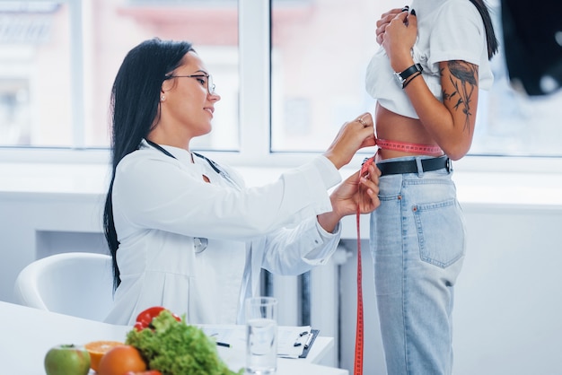 Nutricionista feminina, medindo a cintura do paciente por fita adesiva dentro de casa, no escritório.