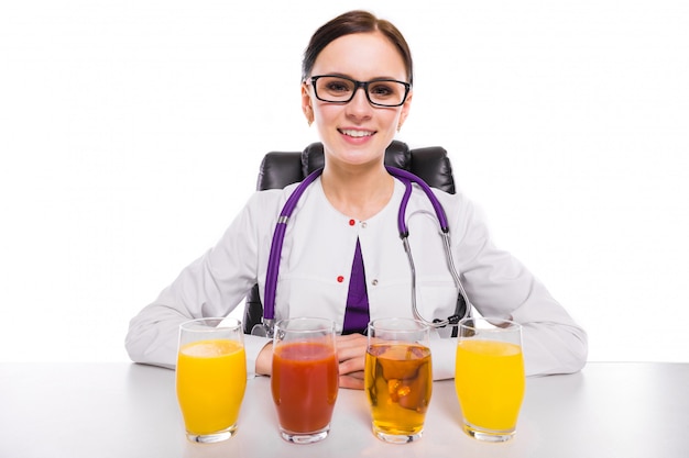 Nutricionista feminina sentada no seu local de trabalho, mostrando e oferecendo copo de suco de tomate de maçã e abacaxi laranja