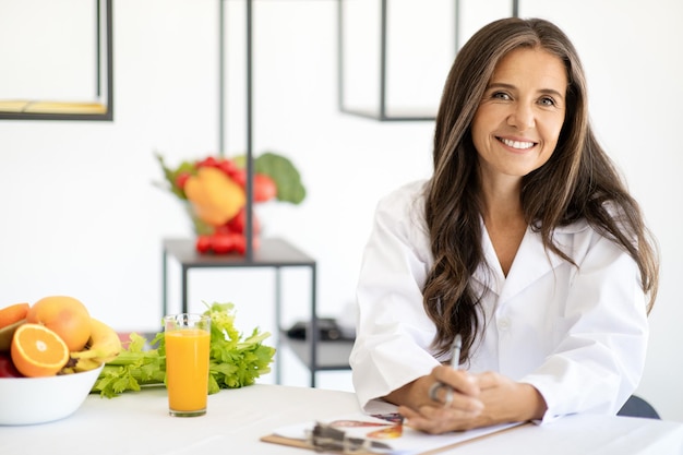 Nutricionista médica europeia adulta feliz em jaleco branco com frutas e legumes orgânicos