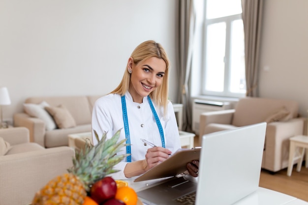 Nutricionista sonriente en su oficina, muestra verduras y frutas saludables, atención médica y concepto de dieta Nutricionista femenina con frutas trabajando en su escritorio