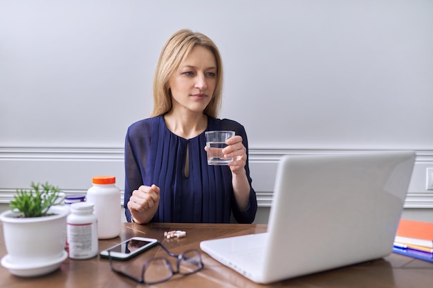 Nutriología nutricionista consultando en línea Mujer profesional mirando la pantalla del portátil hablando con el paciente Mujer mostrando un vaso con agua cápsulas de vitaminas suplementos nutricionales en la mesa