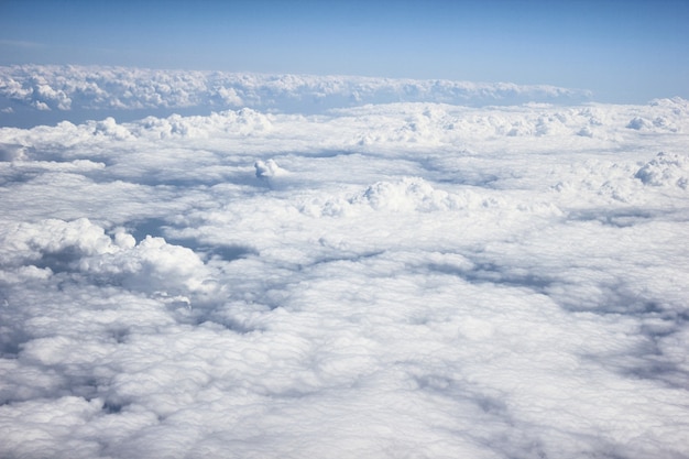 Nuvens brancas / cinzentas pesadas na vista de um avião, com céu azul e luz do sol, um avião está voando acima das nuvens