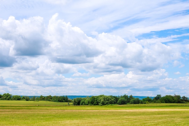 Nuvens brancas contra o céu azul, sobre um campo verdejante.