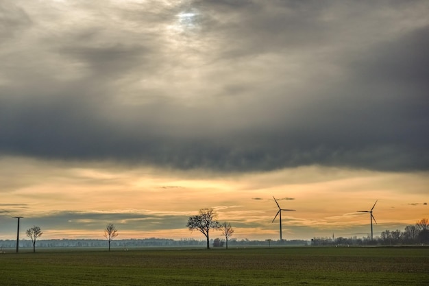 Nuvens cinzentas no céu com moinhos de vento e árvores em uma paisagem plana