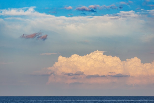 Nuvens cumulus fofas bonitas no céu azul, sol do sol dourado. Paisagem com montanhas e o mar