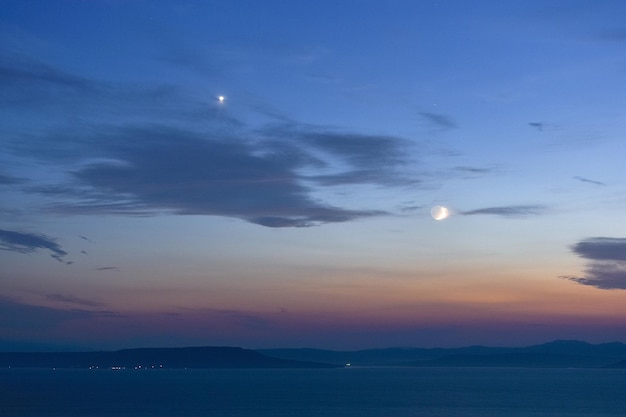 Nuvens e lua no céu azul durante o pôr do sol sobre o mar