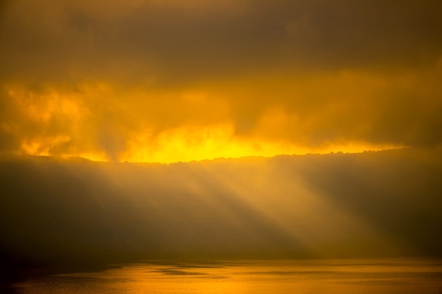 Nuvens pesadas sobre a costa rochosa. Os raios solares mal penetram, iluminam as casas e a superfície da água