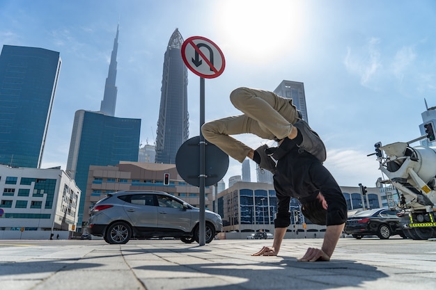 Foto o acrobata flexível mantém o equilíbrio nas mãos com a paisagem urbana de dubai turva e o sinal de trânsito uturn is pr ...