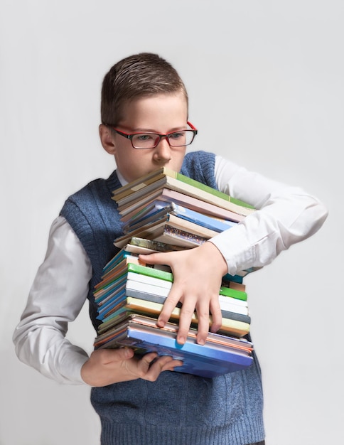 O adolescente bonito e inteligente de óculos carrega uma pilha pesada de livros