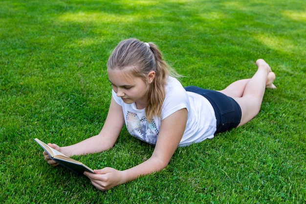 O adolescente bonito encontra-se na grama e lê-se o livro no parque no dia ensolarado do verão.