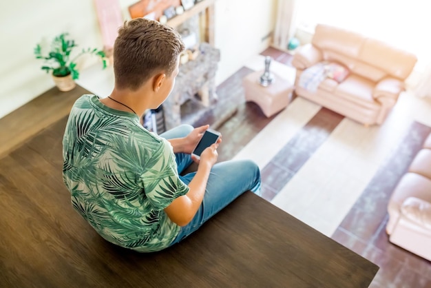 O adolescente está usando celular sentado no segundo andar do topo da casa