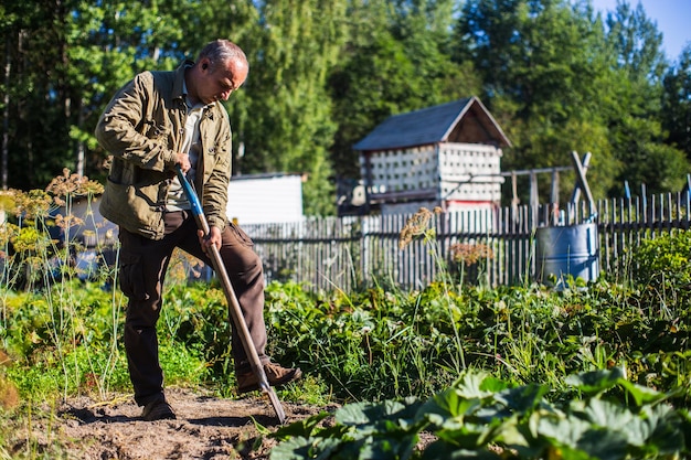 O agricultor cava o solo na horta Preparando o solo para plantar vegetais Conceito de jardinagem Trabalho agrícola na plantação