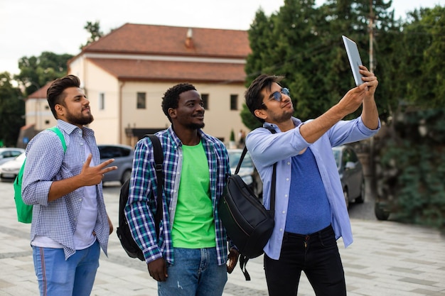 O alegre grupo de estudantes multiétnicos tirando uma selfie ao ar livre