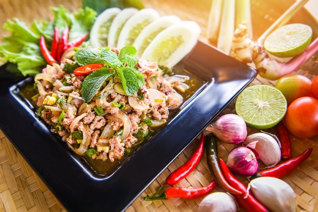 O alimento tailandês triturado picante da salada da carne de porco seriu na tabela com ervas e tempera ingredientes.