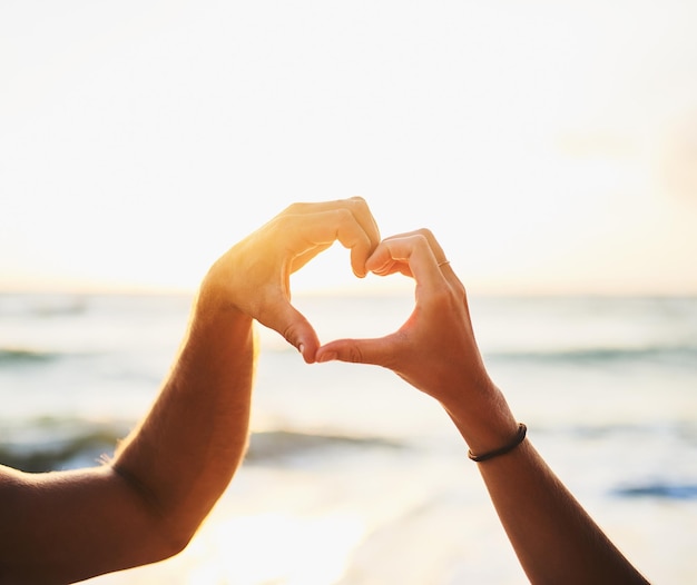 O amor começa comigo e você Foto recortada de um casal formando um coração com as mãos na praia