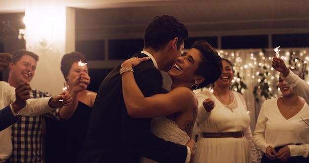 O amor deveria ser sinônimo de felicidade Foto recortada de um afetuoso jovem casal recém-casado dançando enquanto seus convidados seguram estrelinhas na recepção do casamento