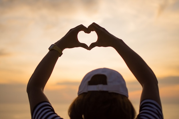 Foto o amor dos pares faz a mão do sinal do coração com por do sol.