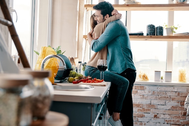 O amor é mais do que apenas um jogo para dois. Lindo casal jovem cozinhando o jantar e bebendo vinho enquanto está na cozinha de casa