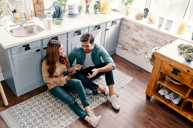 O amor é tudo o que importa. Vista superior de um lindo casal jovem bebendo vinho enquanto está sentado no chão da cozinha em casa