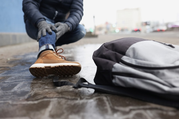 O ângulo baixo do homem atingiu a perna, osso quebrado, chão escorregadio no inverno, preciso de ajuda. Pessoa caiu no asfalto, mochila no chão. Danos, inverno, saúde, acidente, conceito de emergência