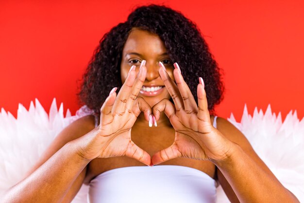 O anjo da mulher com asas mostra o coração das mãos no fundo vermelho