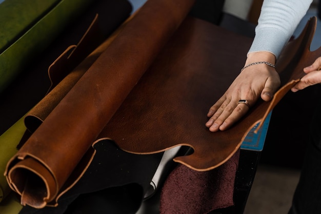 O artesão de couro está tocando o rolo de couro genuíno na oficina Rolos de couro genuíno de cores diferentes na oficina de produtos de couro