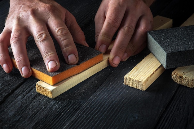 O artesão limpa a prancha de madeira com uma ferramenta abrasiva As mãos do construtor fecham a ideia de renovação ou construção