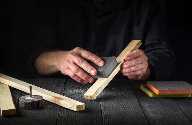 O artesão profissional limpa a prancha de madeira com uma ferramenta abrasiva As mãos do construtor fecham