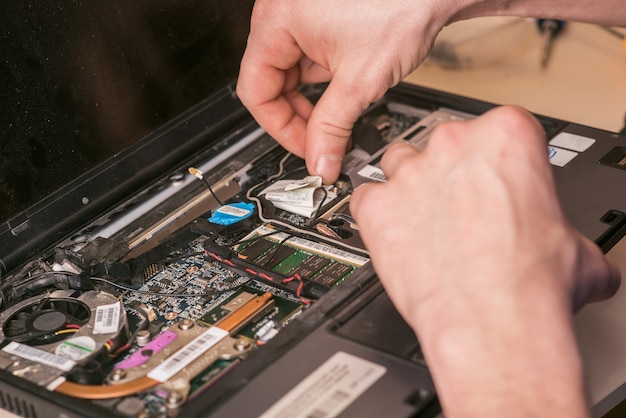 O assistente está consertando o laptop. Desmontagem do laptop para peças de reposição. Manutenção de equipamentos de informática utilizando ferramentas. Vista do laptop dentro