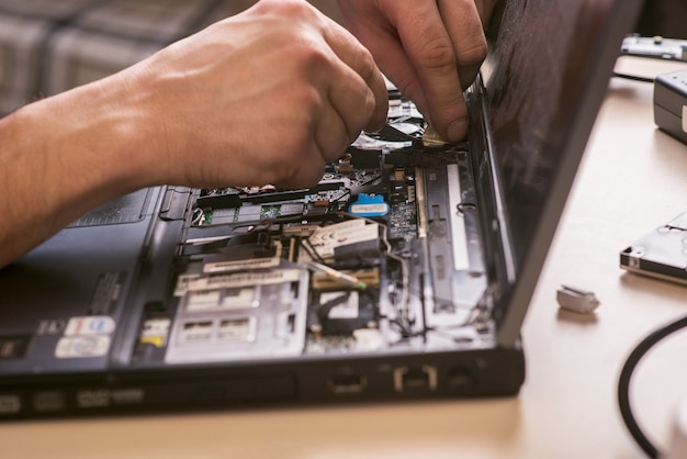 O assistente está consertando o laptop. Desmontagem do laptop para peças de reposição. Manutenção de equipamentos de informática utilizando ferramentas. Vista do laptop dentro