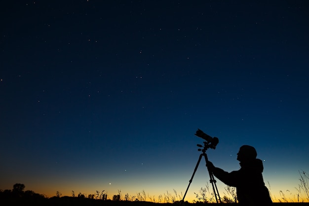 O astrônomo fotografa o céu estrelado à noite em uma câmera digital usando um tripé.