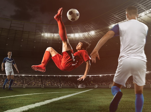 Foto o atacante de futebol com uniforme vermelho acerta a bola com um chute acrobático para o alto no estádio