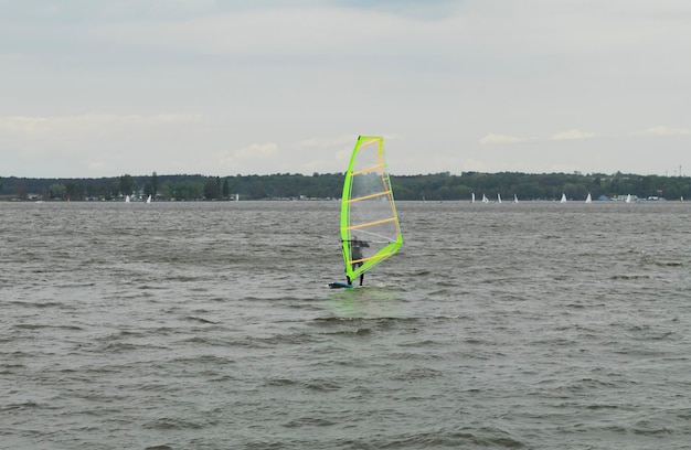 O atleta patina em uma prancha com uma vela na água O kitesurfer anda na água em um pequeno lago